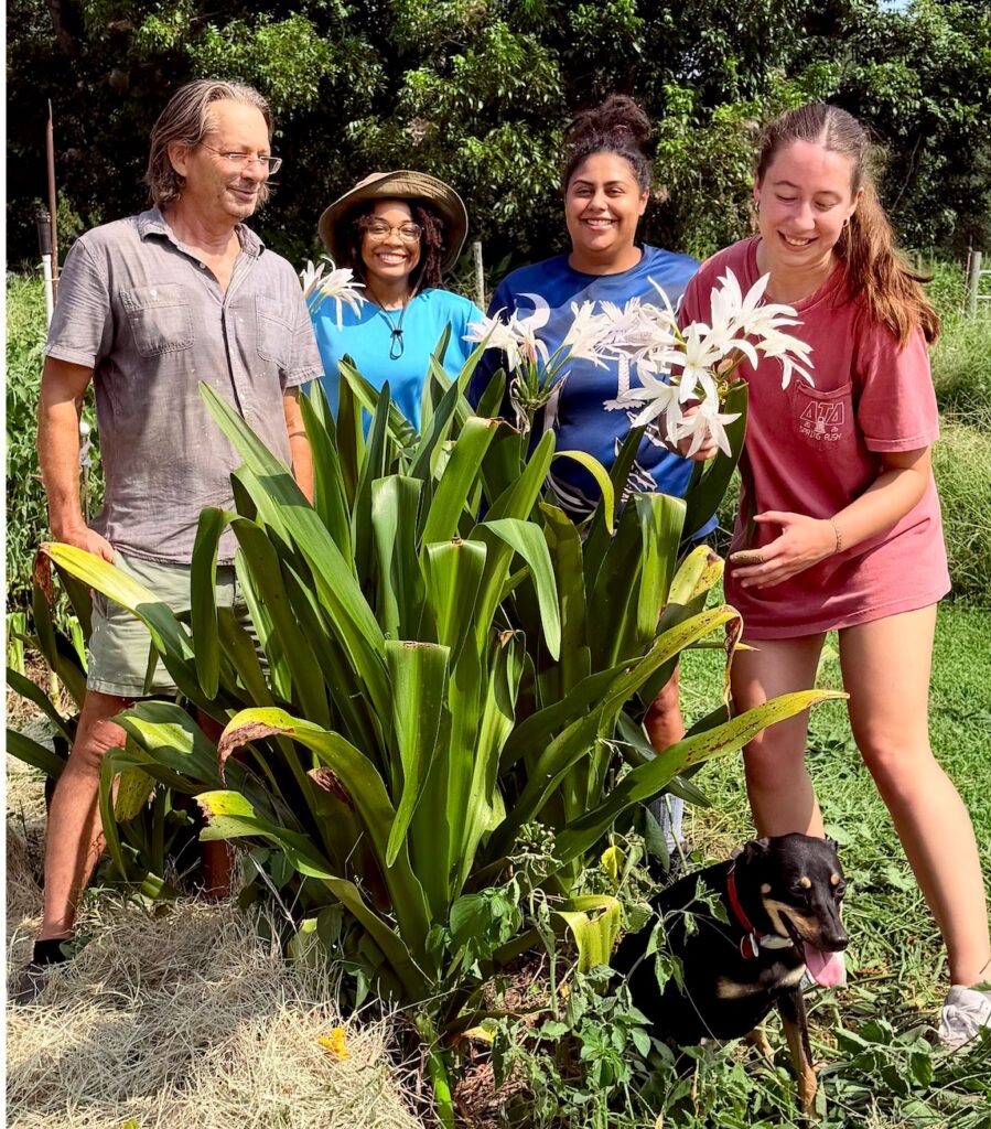 Jenks Farmer team standing with a huge Crinum x 'Candace' plant covered in fragrant white blooms, a zone 8 tough plant for August gardens